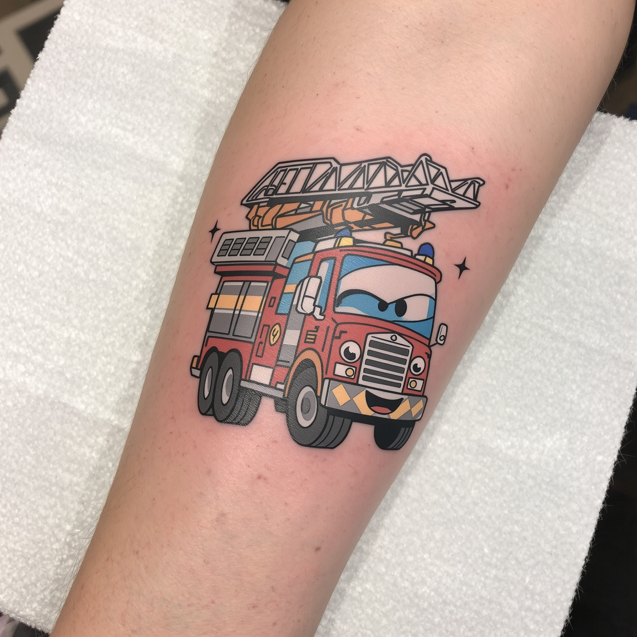 Vibrant New School tattoo of a cartoon fire truck with exaggerated features, showcasing dynamic lines and a playful expression on the forearm.